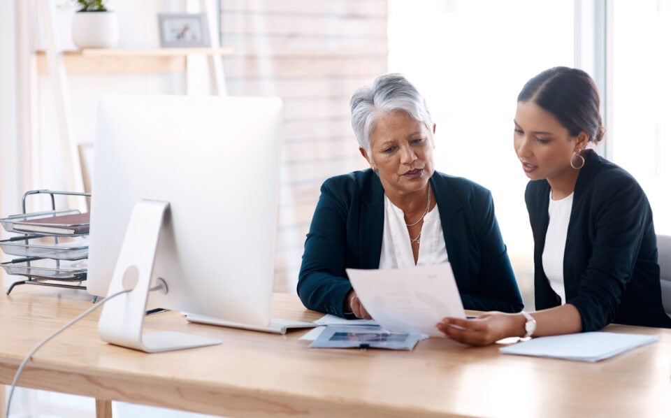 Mentor, coaching or business women with paperwork talking, speaking or planning project in office. Documents, teamwork collaboration or senior manager reading with intern for administration training.